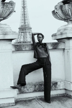 Black and white portrait of a model in Paris. She is wearing a dark, textured top and pants with the Eiffel Tower in the background.