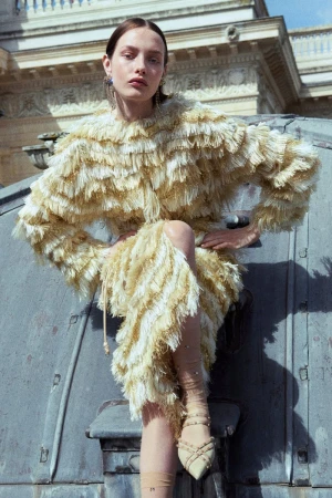 Model Clara Denison poses in a tiered yellow and cream fringe dress on an architectural zinc rooftop for Ulla Johnson.