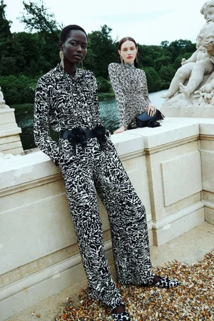 Two female models in printed matching outfits posing near a stone balustrade with a river and park background for Ulla Johnson