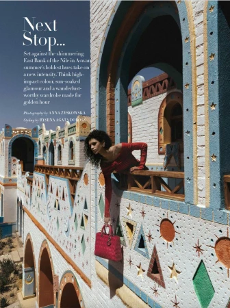 Woman leaning over a painted balcony railing holding a pink handbag in Aswan, for Harper's Bazaar Arabia