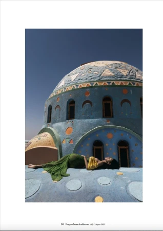 Model lying on a blue domed rooftop wearing a green dress against a clear sky for Harper's Bazaar Arabia