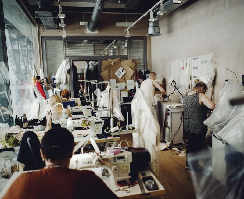 Designers and assistants working in a fashion atelier with industrial sewing machines, fabric rolls, and pattern papers.