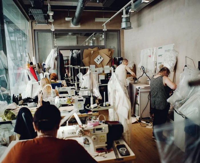 Designers and assistants working in a fashion atelier with industrial sewing machines, fabric rolls, and pattern papers.