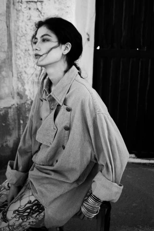Monochrome portrait of model Vanessa Pompucci seated outdoors in an oversized collared jacket and patterned tights for Grey Magazine.