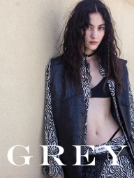 Model Vanessa Pompucci wearing a black leather vest over a wavy black and white patterned shirt leaning against a beige wall.