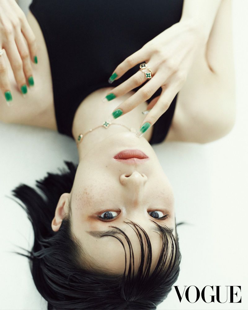 An upside-down portrait of model Esther Kim lying down with green manicured nails, black sleeveless top, and fine jewelry for Vogue Korea.