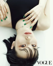 An upside-down portrait of model Esther Kim lying down with green manicured nails, black sleeveless top, and fine jewelry for Vogue Korea.