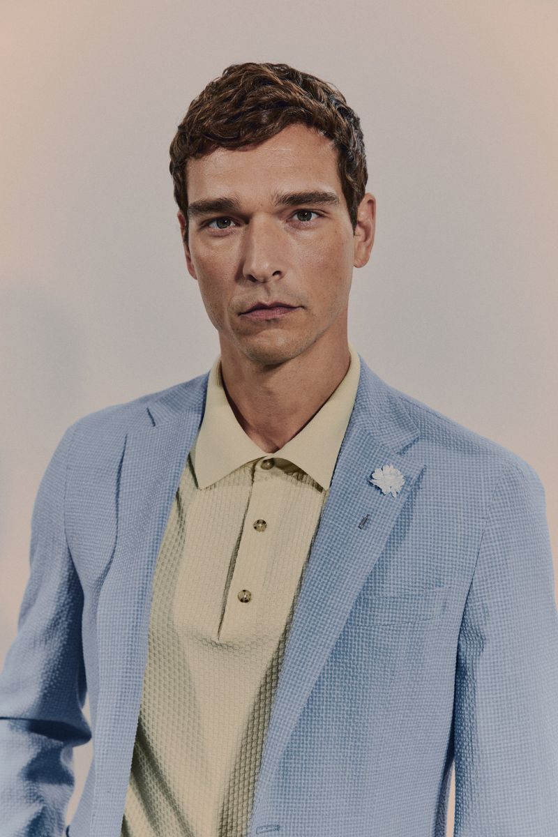 Adult man wearing light blue blazer and tan polo shirt, in a studio shot. Portrait of a handsome man in smart casual clothing.