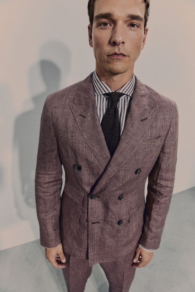 Man in a mauve-colored suit and striped shirt with a dark tie, posing indoors in a double-breasted jacket and matching pants.