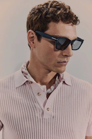 Portrait of a light-skinned adult male wearing dark sunglasses and a pink polo shirt, posing in a photo studio against a neutral backdrop.