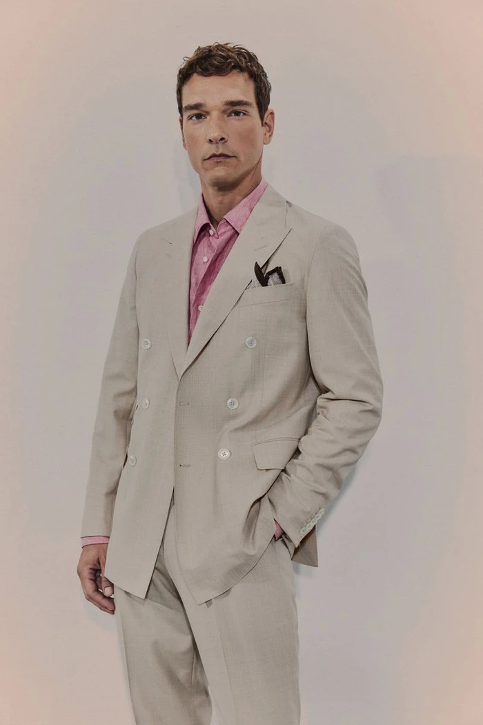 Model Alexandre Cunha wearing a beige double-breasted suit and pink collared shirt against a neutral studio backdrop.