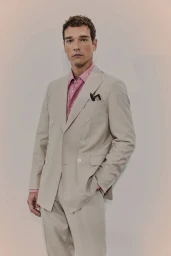 Model Alexandre Cunha wearing a beige double-breasted suit and pink collared shirt against a neutral studio backdrop.