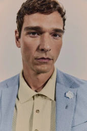 Model Alexandre Cunha in a light blue textured suit jacket and pale yellow knit polo against a neutral backdrop.