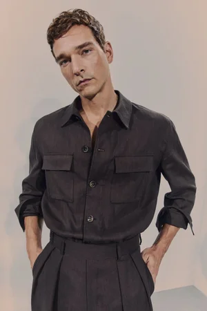 Model Alexandre Cunha wearing a dark grey button-down shirt and trousers against a neutral studio backdrop for BOSS.