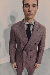 Alexandre Cunha wearing a textured double-breasted suit, striped shirt, and dark tie in a high-angle studio portrait.