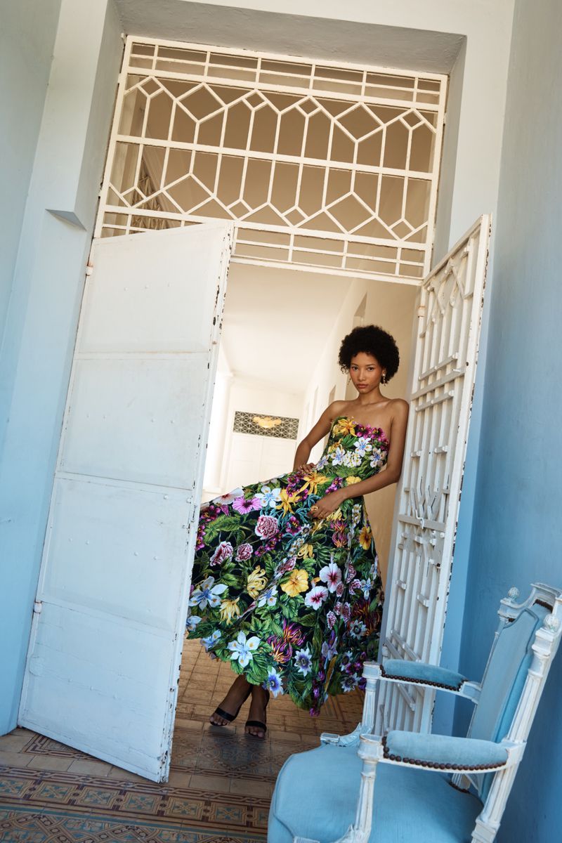 Model wearing a vibrant floral strapless dress posing inside an ornate doorway for Oscar de la Renta Pre-Fall 2026
