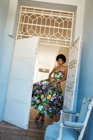 Model wearing a vibrant floral strapless dress posing inside an ornate doorway for Oscar de la Renta Pre-Fall 2026