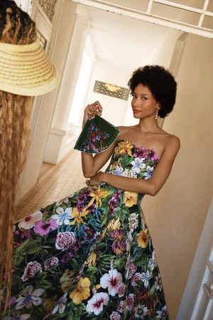 Model Lineisy Montero in a strapless floral gown holds a matching fan in a sunlit hallway for Oscar de la Renta Pre-Fall 2026.