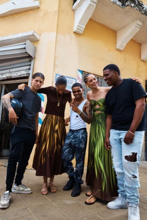 Group of five people laughing together on an outdoor street, including models in printed Oscar de la Renta dresses.