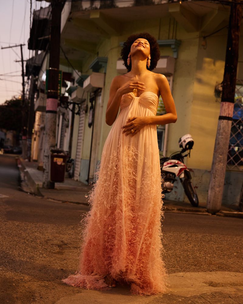 Model wearing a strapless pink feathered gown posing outdoors on a street at dusk