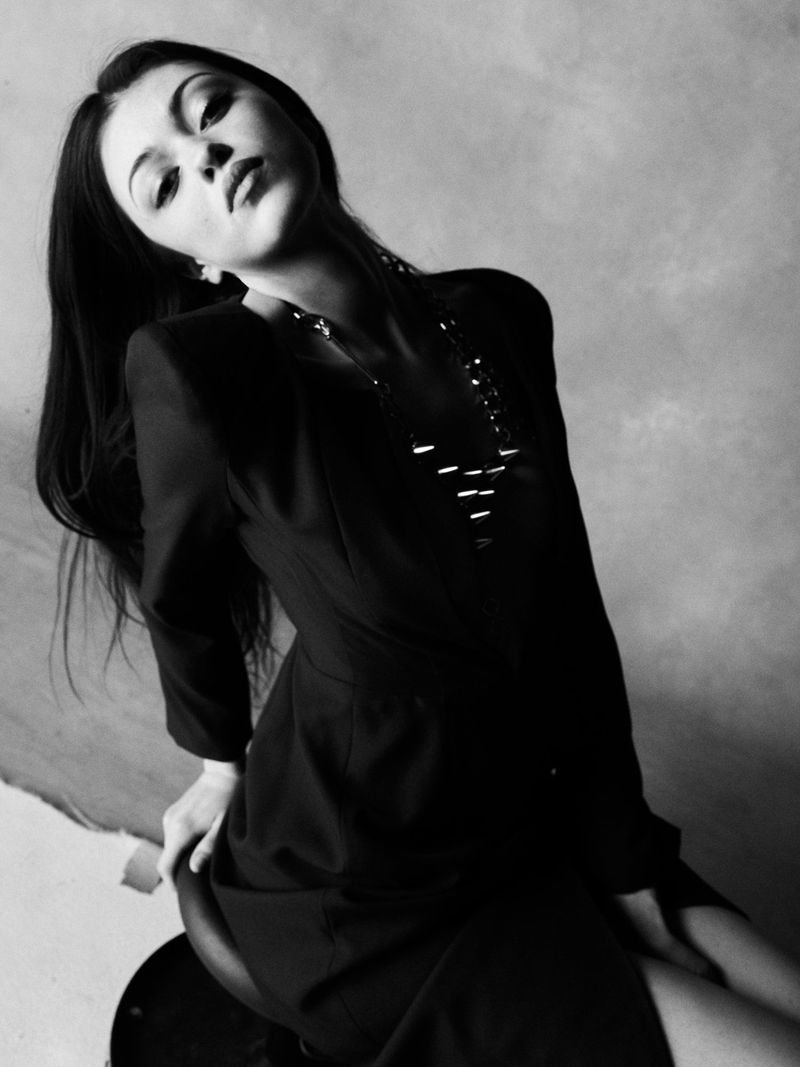 Monochrome portrait of model Jules Santiago wearing a black tailored blazer and statement necklace against a studio backdrop.