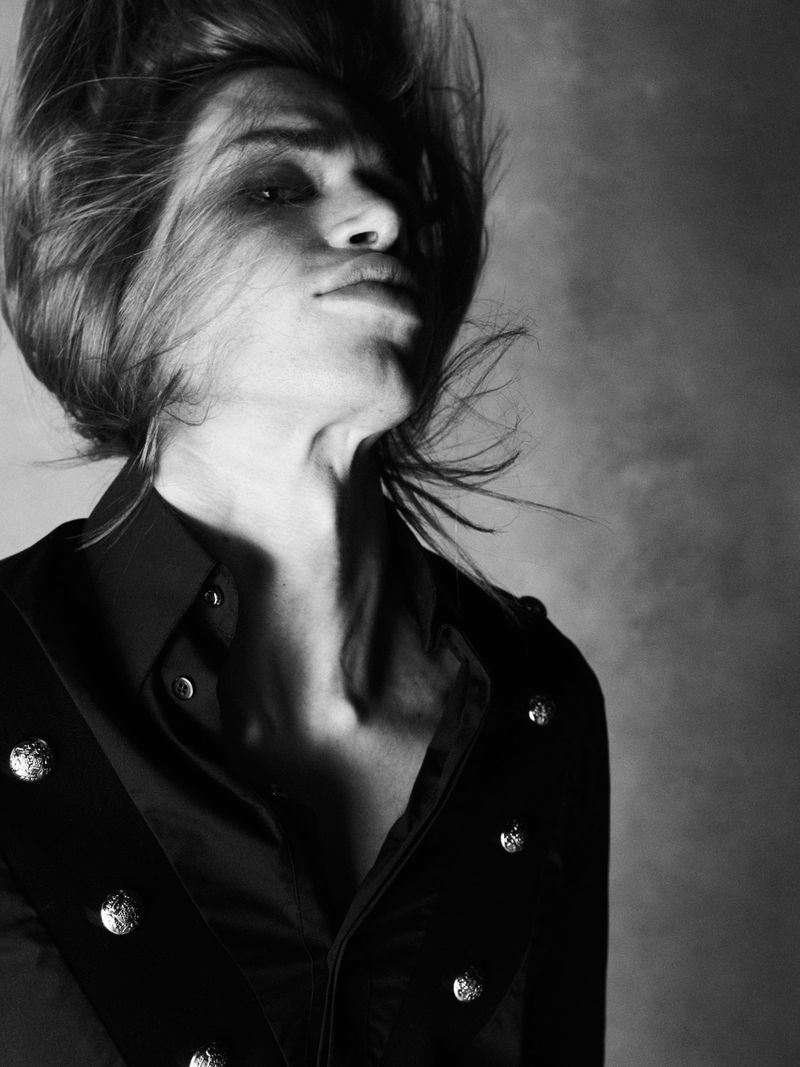 Monochrome portrait of model Jules Santiago with dynamic windblown hair wearing a black buttoned shirt against a textured backdrop.