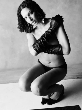 Model Jules Santiago crouching in long black leather gloves and briefs against a studio backdrop in black and white.