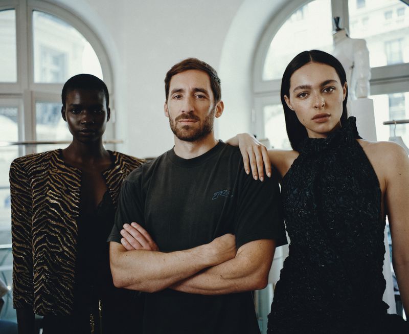 Designer Antonin Tron standing between models Rodah Nyahouw and Amelie Zalaiti in a fashion atelier.