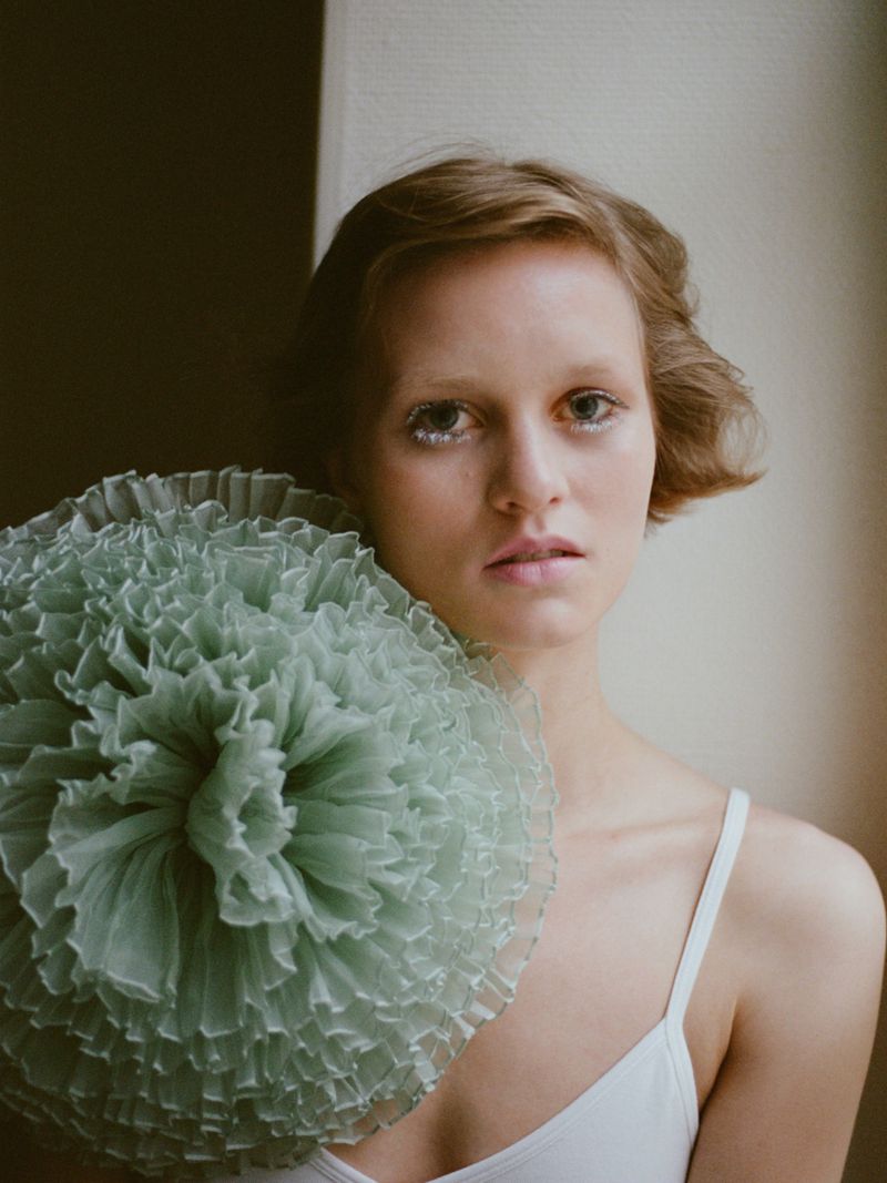 Model Sofia Hansson holding a large ruffled sage green tulle pom-pom wearing a white strap top.