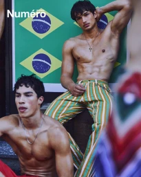 Shirtless male model in striped trousers posing against Brazilian flags for Numéro Istanbul Homme editorial.