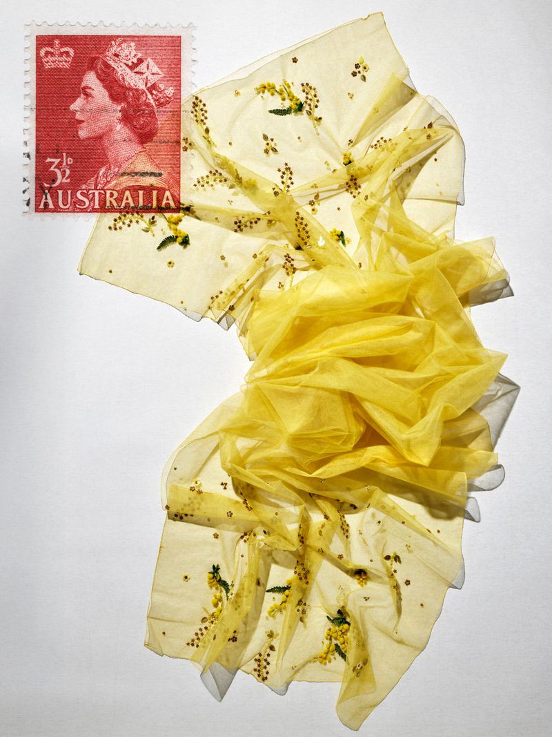 Red Australian postage stamp of Queen Elizabeth II alongside draped sheer yellow embroidered fabric on a white surface.