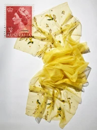 Red Australian postage stamp of Queen Elizabeth II alongside draped sheer yellow embroidered fabric on a white surface.