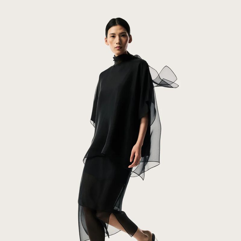 Model Jiayun Xie wearing a layered sheer black high-neck outfit against a plain off-white studio background.