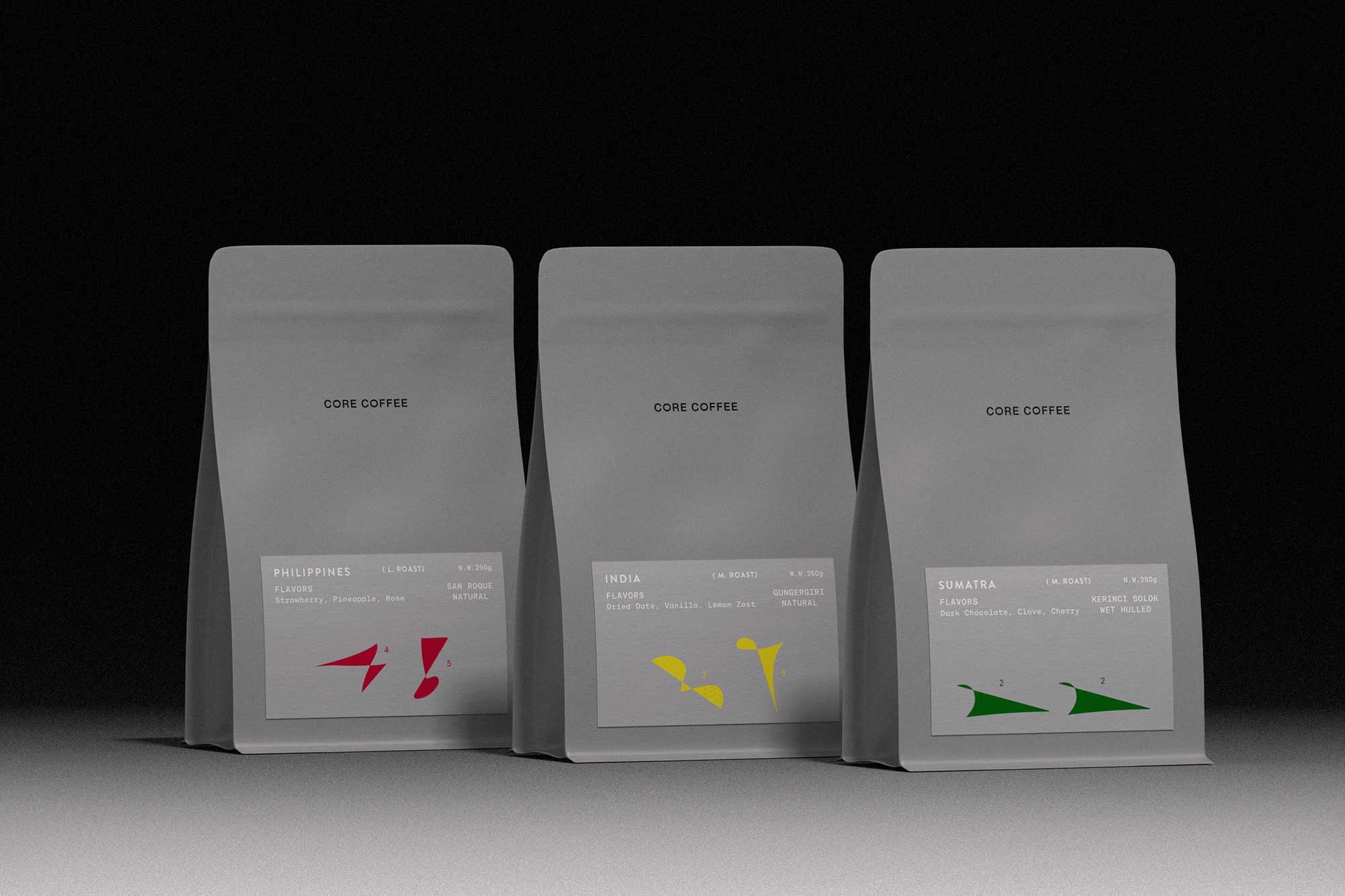 Three grey CORE COFFEE pouches standing in a row with minimalist labels and colorful geometric accents against a dark backdrop.