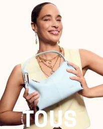 Brandi Quinones smiles while holding a light blue leather Tous handbag against a plain off-white studio background.