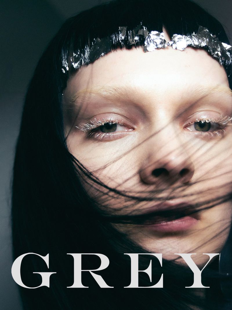 Dramatic close-up of a woman with silver foil headpiece, white eyebrows, and dark hair partially obscuring her face, for beauty or fashion.