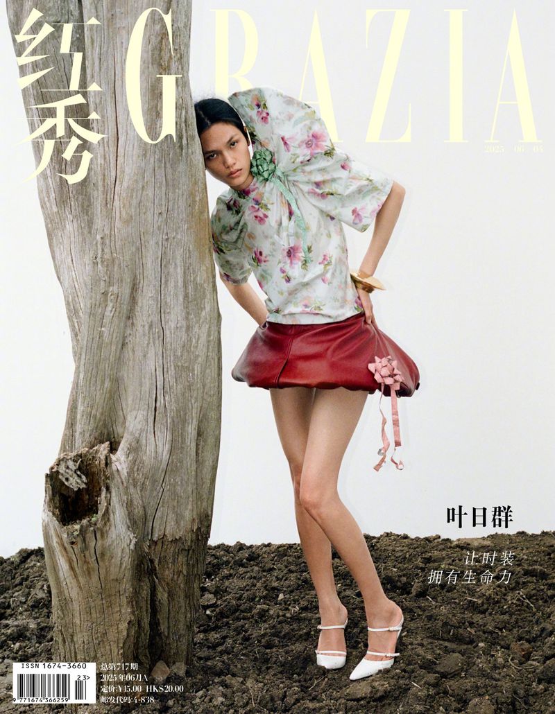 Fashion editorial shot of a model posing with a tree trunk, wearing a floral blouse and red skirt, featured in Grazia magazine.
