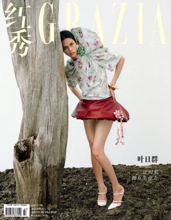 Fashion editorial shot of a model posing with a tree trunk, wearing a floral blouse and red skirt, featured in Grazia magazine.