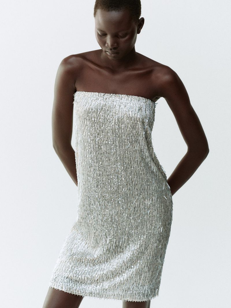 Model Aluel Keror wearing a strapless silver sequined mini dress against a plain white studio background.