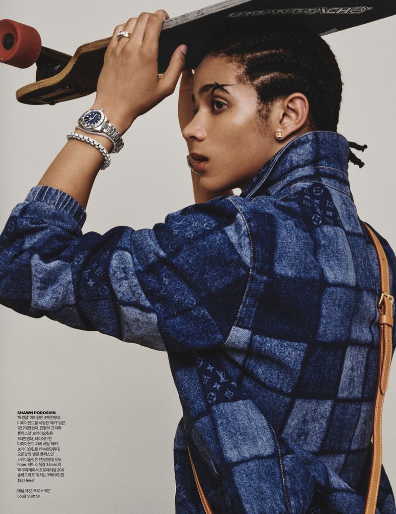 Side profile of a man holding a skateboard overhead wearing a blue patchwork denim jacket and silver watch.