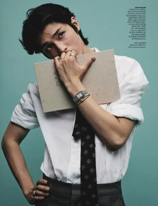 East Asian male model holding a notebook in front of his face in a white shirt and dark patterned tie against a teal background.