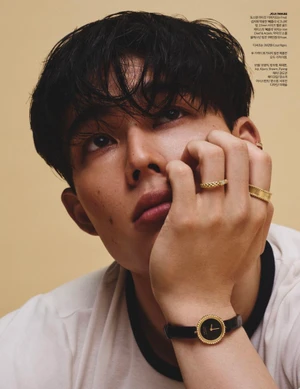 Close-up portrait of model Joji Iwase resting his chin on his hand while wearing gold rings and a black strap wristwatch.