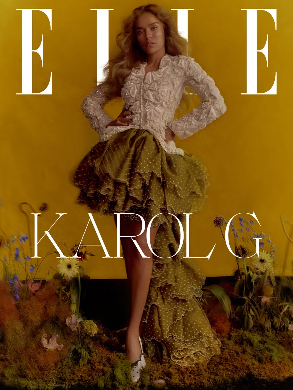 Karol G wearing a textured white top and ruffled olive skirt amid a faux floral garden for Elle U.S.