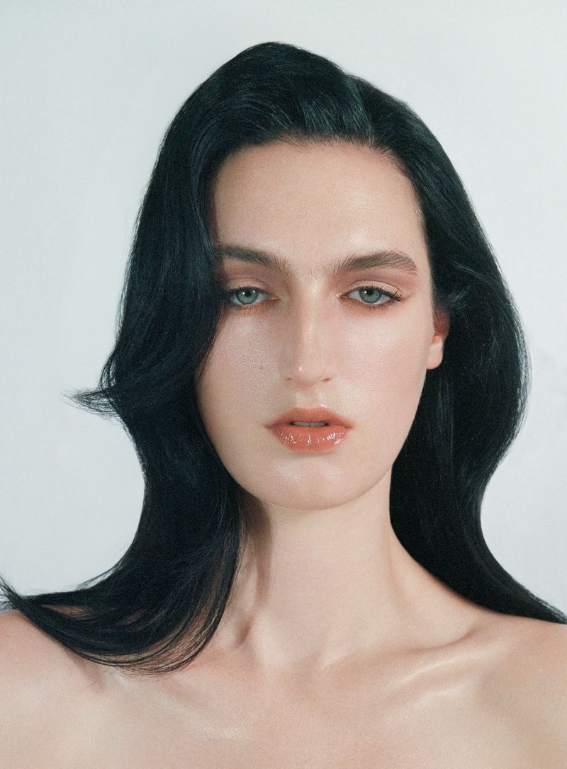 Close-up beauty portrait of a woman with long dark hair and natural makeup against a plain white background