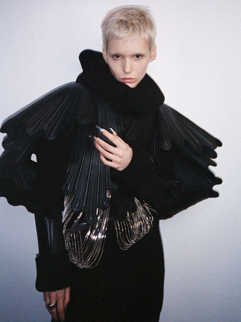 Model Paulina Bricca posing in a sculptural black jacket with layered shoulder details and metallic fringe for Elle Kazakhstan.