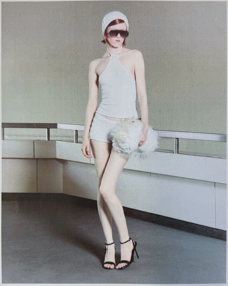 Model in white halter top and shorts holding a fluffy white bag against a grey wall