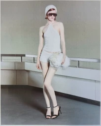 Model in white halter top and shorts holding a fluffy white bag against a grey wall