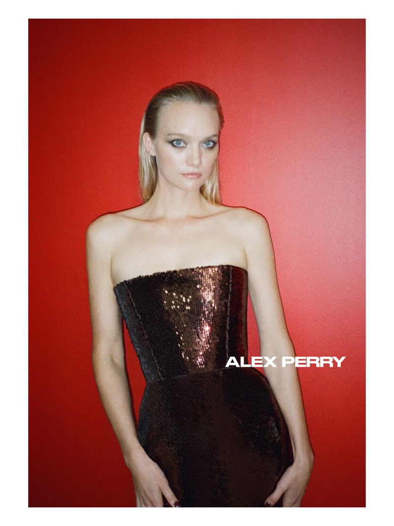 Model Gemma Ward wearing a strapless bronze sequin dress against a bold red studio backdrop for Alex Perry.