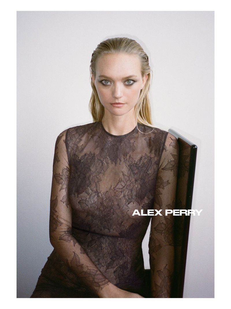 Model Gemma Ward seated in a sheer brown floral lace long-sleeve dress against a neutral studio backdrop for Alex Perry.