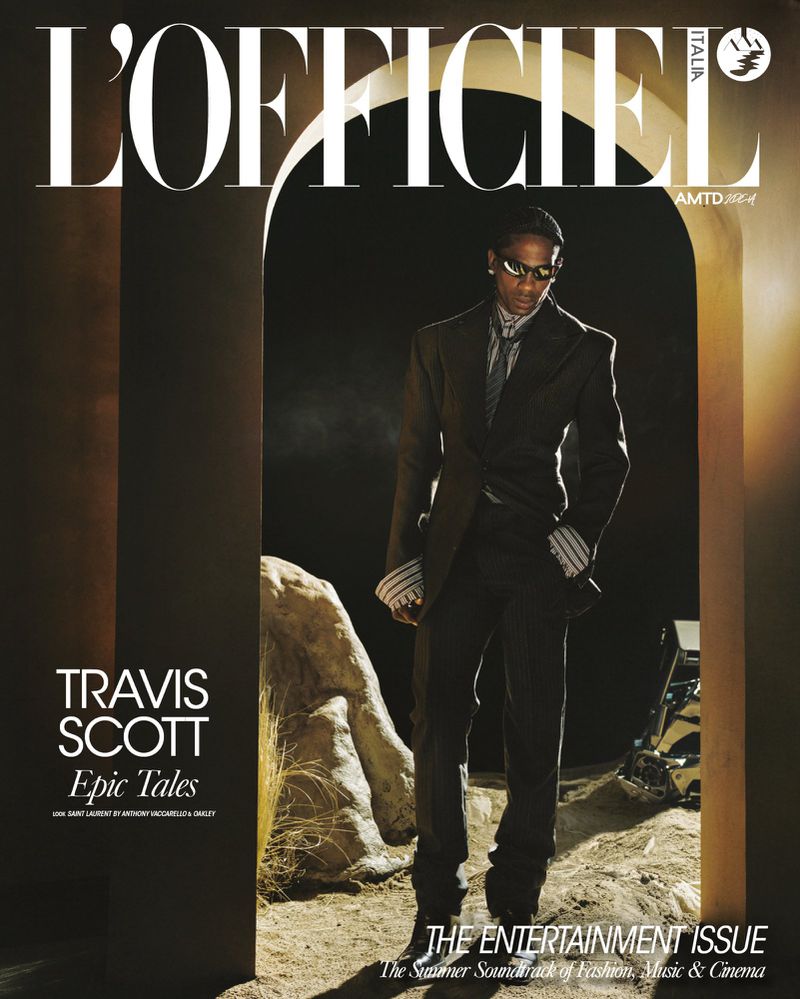 Travis Scott wearing a dark tailored suit and sunglasses, standing inside an arched doorway on a desert set for L'Officiel Italia.